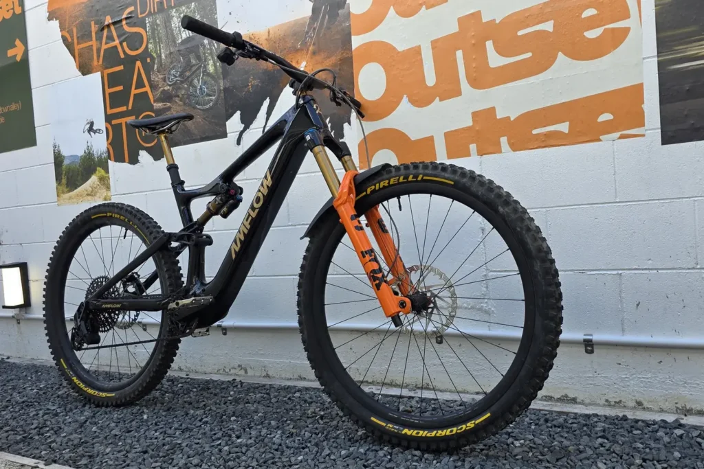 Black full-suspension mountain bike with an orange fork in front of the Outset mural