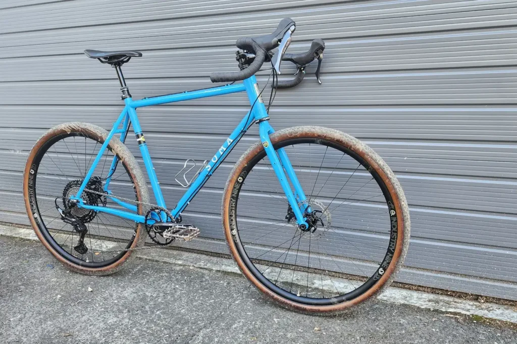 Blue gravel bike with tan-wall tyres and drop bars, built by Outset