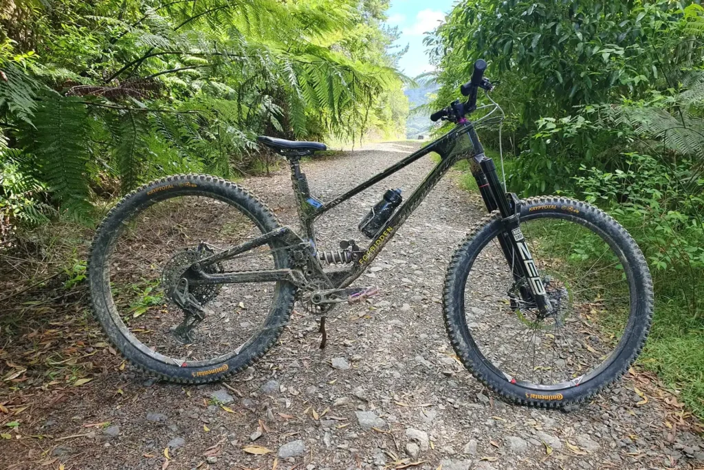 Full-suspension mountain bike built by Outset on a gravel track through native bush