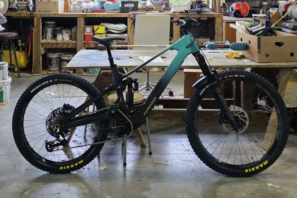 Teal and black full-suspension mountain bike in the Outset workshop